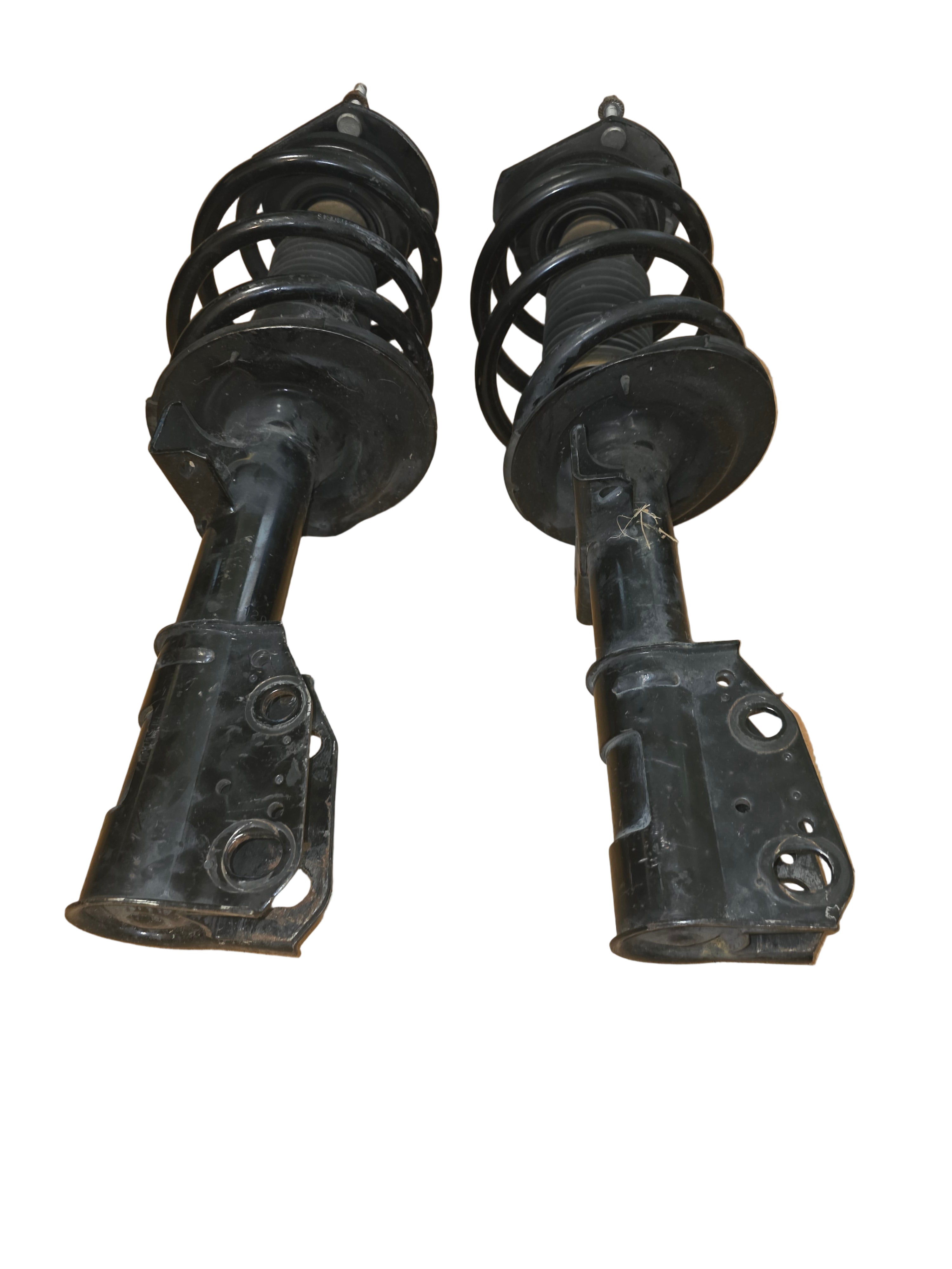 Two black automotive shock absorbers on a wooden floor.