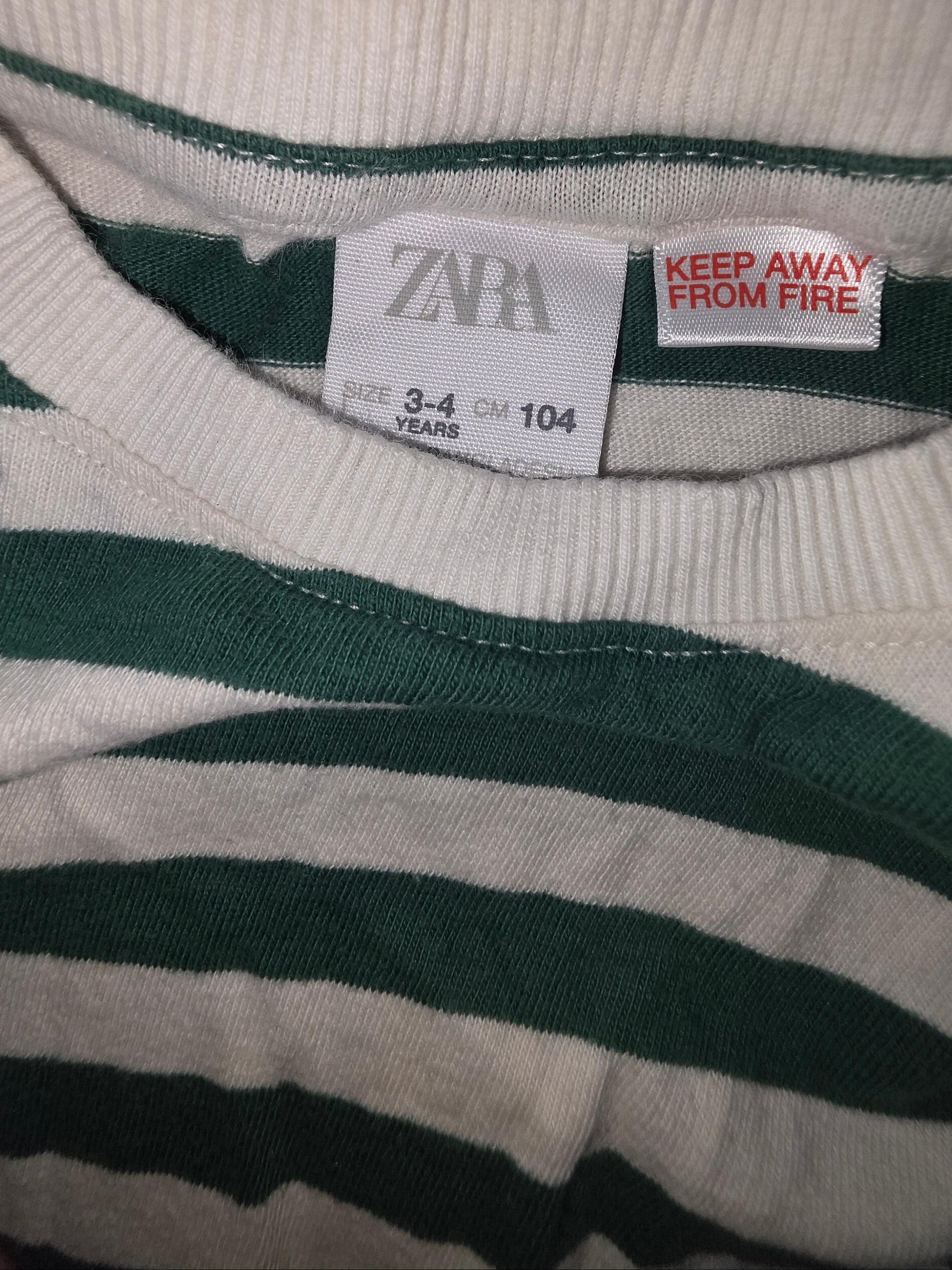 Close-up of a Zara label on a striped garment with a warning tag.